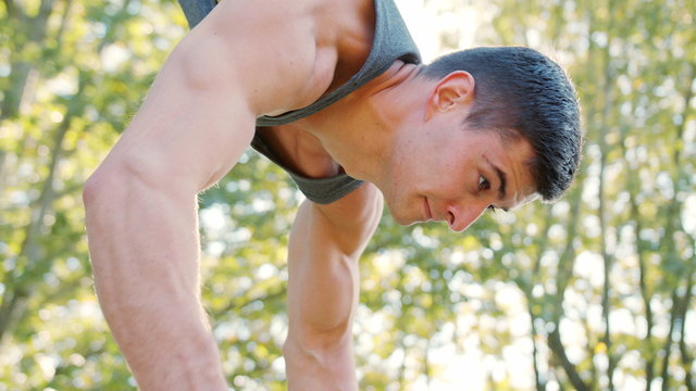 Male athlete performing difficult exercise on gymnastic parallel bars. Slim athlete a very fit guy fitness instructor or a personal trainer working out his arm muscles on outdoor beach gym as part of