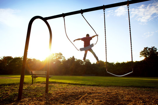 Boy jumping from swing at park during sunset