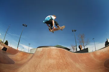 Fotobehang Skateboard Low angle view of man jumping with skateboard at skate ramp against blue sky  © Cavan for Adobe