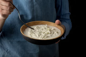 Fotobehang Zuivelproducten Woman in blue apron holding bowl with stracciatella mozzarella cheese on dark background