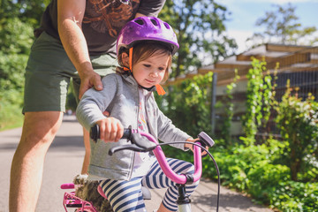 father teaches little toddler daughter to ride a bike in the park