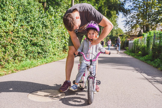 father teaches little toddler daughter to ride a bike in the park