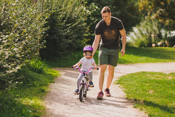 father teaches little toddler daughter to ride a bike in the park