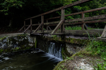 Fototapeta na wymiar Small waterfall under wooden bridge in nature. Long exposure shot. Motion water 