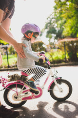 father teaches little toddler daughter to ride a bike in the park