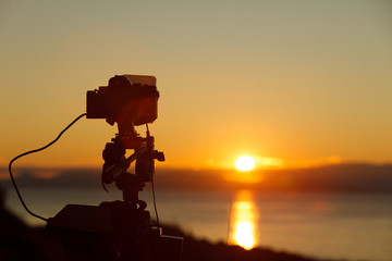 Camera taking picture of sunrise over sea surface