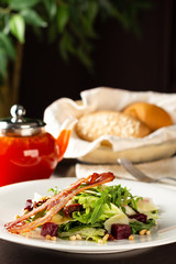 Salad with bacon and vegetables close-up on a wooden table