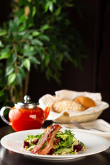 Spicy bacon salad, tomato, nuts and lettuce close-up on a plate on the table. Vertical view