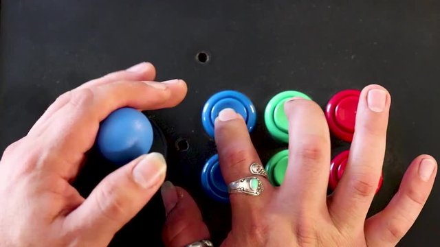 A realtime over head close up shot of a man playing video game by controlling joystick and pressing various buttons with his hands