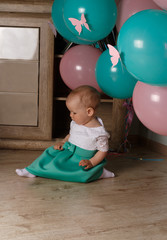 Fototapeta premium little girl sitting on the floor in the room next to the balloons, first birthday, celebrate. one year old blue and pink balls with butterflies. girl in white and blue dress