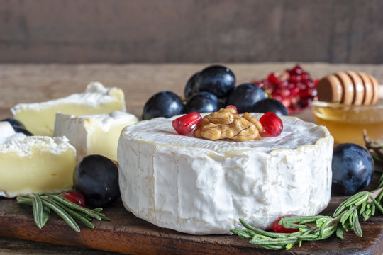 delicious camembert cheese with grapes, pomegranate seeds, honey walnuts and rosemary on wooden cutting board