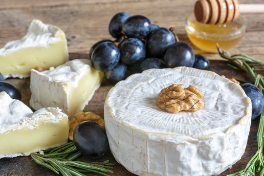 camembert cheese with grapes, honey walnuts and rosemary on wooden cutting board