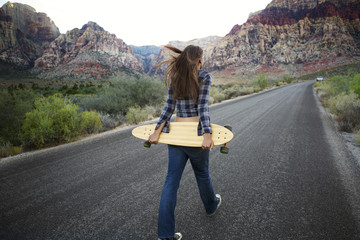 Woman carrying skateboard while walking on mountain road © Cavan for Adobe