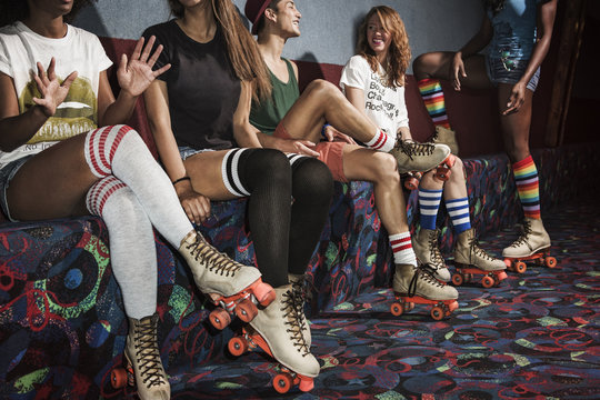 Friends wearing roller skates sitting on multi colored sofa at roller rink