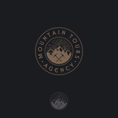 Mountain tours logo. Travel agency emblem. Gold mountains and ice axes on a circle. Emblem for alpinism, ski resort or mountain tourism. Monochrome option.