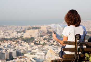 Fototapeta na wymiar woman with a map sitting on Lycabettus Hill, the highest point in the city overlooking Athens with the Acropolis - world traveller