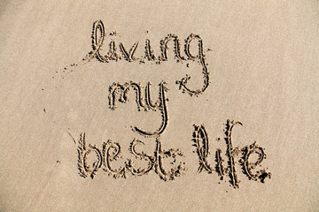 The words 'living my best life' written in sand on a beach