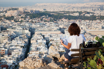 Fototapeta na wymiar woman with a map sitting on Lycabettus Hill, the highest point in the city overlooking Athens with the Acropolis - world traveller
