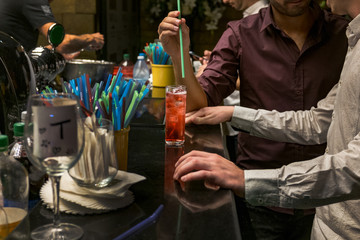 Two man  are standing at a bar counter and holding  glass with an alcoholic cocktail  Red cocktail in a glass at a nightclub, beach, restaurant