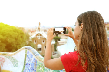Back view of woman taking picture of Park Guell and landscape from terrace of the park, Barcelona, Spain