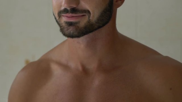 Bearded man applying perfume on neck in bathroom, special fragrance for men