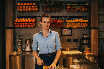 Happy young female bartender standing at juice bar counter and working.
