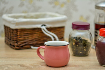 Drink tea for breakfast. A cup of tea, a jar of tea petals, a jar of jam and a basket for cookies.