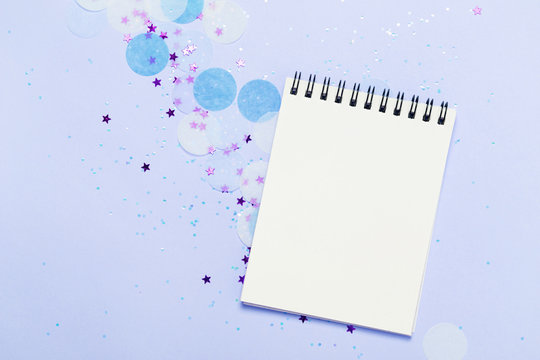 Empty note pad on blue frozen festive background with confetti and sparkles.