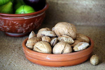 Small ceramic bowl of walnuts and almonds, with a bowl of figs in the background