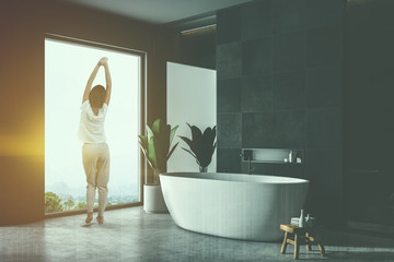 Woman in black tile bathrom corner, tub