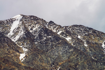 Snowy mountain top in cloudy sky. Rocky ridge under clouds. Overcast weather in highlands....