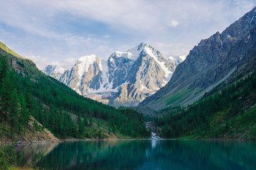 Fototapeta na wymiar Wonderful giant snowy mountains. Creek flows from glacier into mountain lake. Reflection in water in highlands. White clear snow on ridge. Amazing atmospheric landscape of majestic Altai nature.