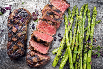 Traditional barbecue dry aged sliced roast beef steak with green asparagus as top view on an old...