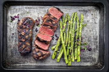 Traditional barbecue dry aged sliced roast beef steak with green asparagus as top view on an old backing form