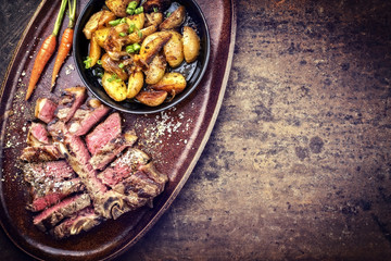 Barbecue dry aged wagyu porterhouse steak sliced with fried potatoes as top view on a plate