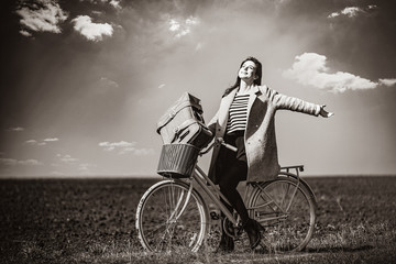 portrait of a young woman with a bicycle and suitcase standing in the middle of the field. Image in black and white color style - Powered by Adobe