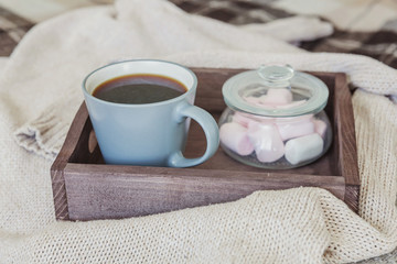 Obraz na płótnie Canvas Cup of coffee on rustic wooden tray, sweet marshmallow and warm woolen sweater. Cozy autumn or winter weekend or holidays at home. Fall home decoration with hot drink mug. Hygge morning style concept