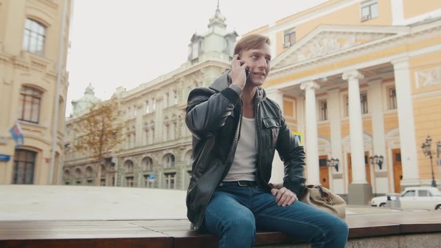 Young brutal man talking on the phone in a European city. Slo-mo