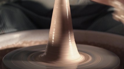 Experienced potter shapes the clay product - jug - with pottery tools. Close up of male hands working on potter's wheel. Shot of half-finished ceramic vase spinning on jigger