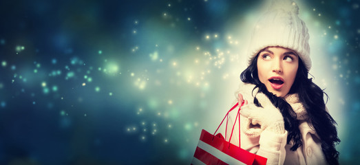 Happy young woman holding a shopping bag in snowy night