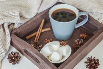 Cup of coffee on rustic wooden tray, sweet marshmallow and warm woolen sweater. Cozy autumn or winter weekend or holidays at home. Fall home decoration with hot drink mug. Hygge morning style concept