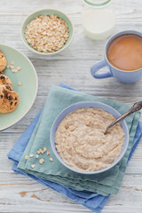 Oatmeal porridge bowl on the white wooden background.