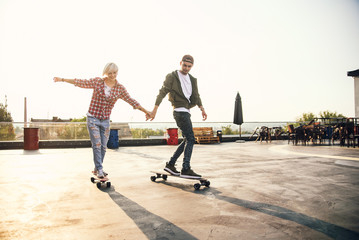 Handsome young couple having fun with skateboards on the roof of industrial building. Modern urban...