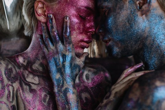 Closeup portrait of couple of girls with bright pink and blue shiny bodyart embracing each other with closed eyes