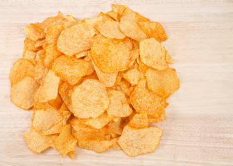 Pile of baked bbq potato chips in a pile on light wood table. Flat lay top view.