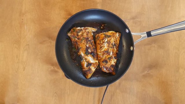 Person sues spatula on fish in pan, close up