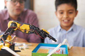 Closeup of a robotic arm with boy and adult in the background