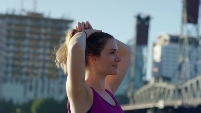 Athlete Pulls Her Hair Up Into Ponytail, Getting Ready For Workout, Cityscape Behind Her