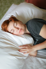 Close portrait of Redhead sleeping adult woman lies in white bed with eyes closed