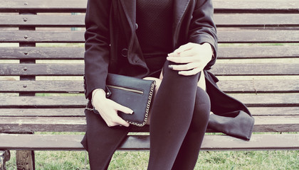 Fashion teen holding black clutch sitting on park bench in spring time. Instagram style